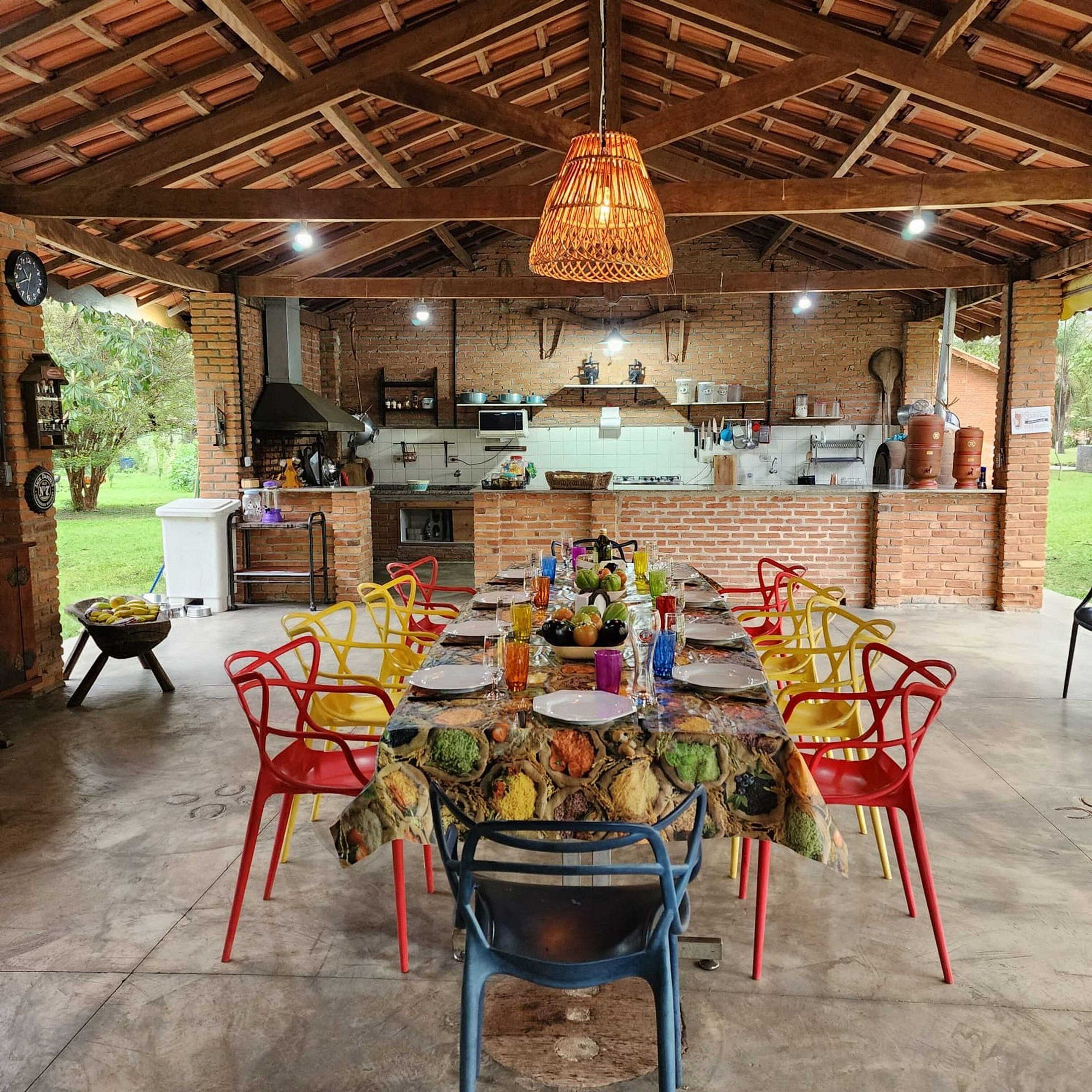 Una cocina exterior con pared de ladrillo, una lámpara colgante y un comedor con sillas coloridas y una mesa dispuesta para una comida.
