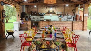 Una cocina exterior con pared de ladrillo, una lámpara colgante y un comedor con sillas coloridas y una mesa dispuesta para una comida.
