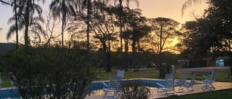 Ein Poolbereich mit Liegestühlen und Blick auf Bäume bei Sonnenuntergang.