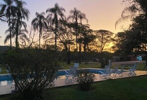A pool area with lounge chairs and a view of trees at sunset. - Magnífico Rancho em Jarinu (Jarinu)