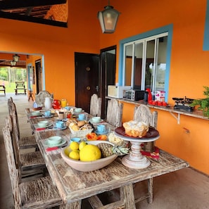 A long dining table set with various dishes and drinks, a bowl of fruit, and a vintage radio. - Magnífico Rancho em Jarinu (Jarinu)