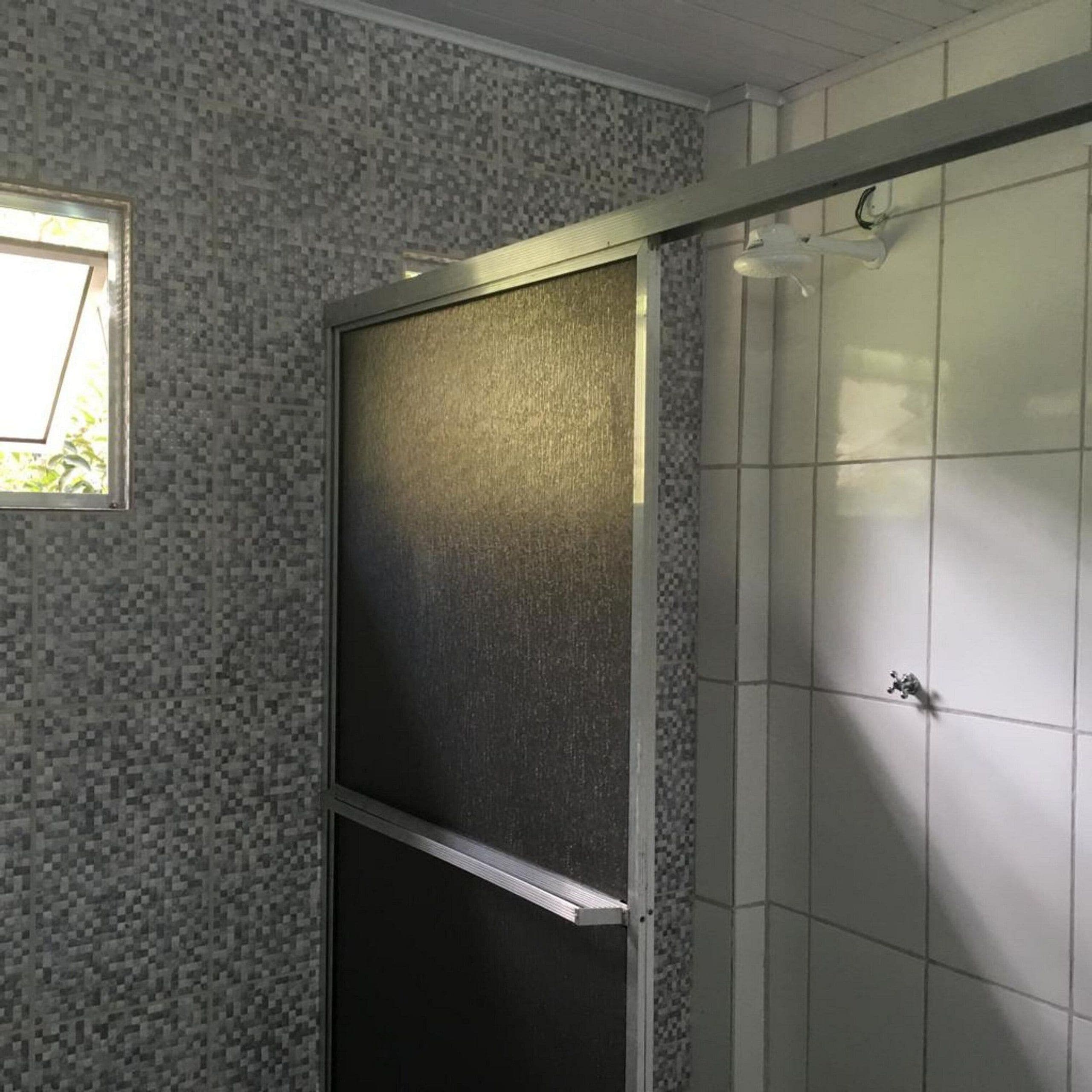A bathroom with a tiled wall, a window, and a shower area.