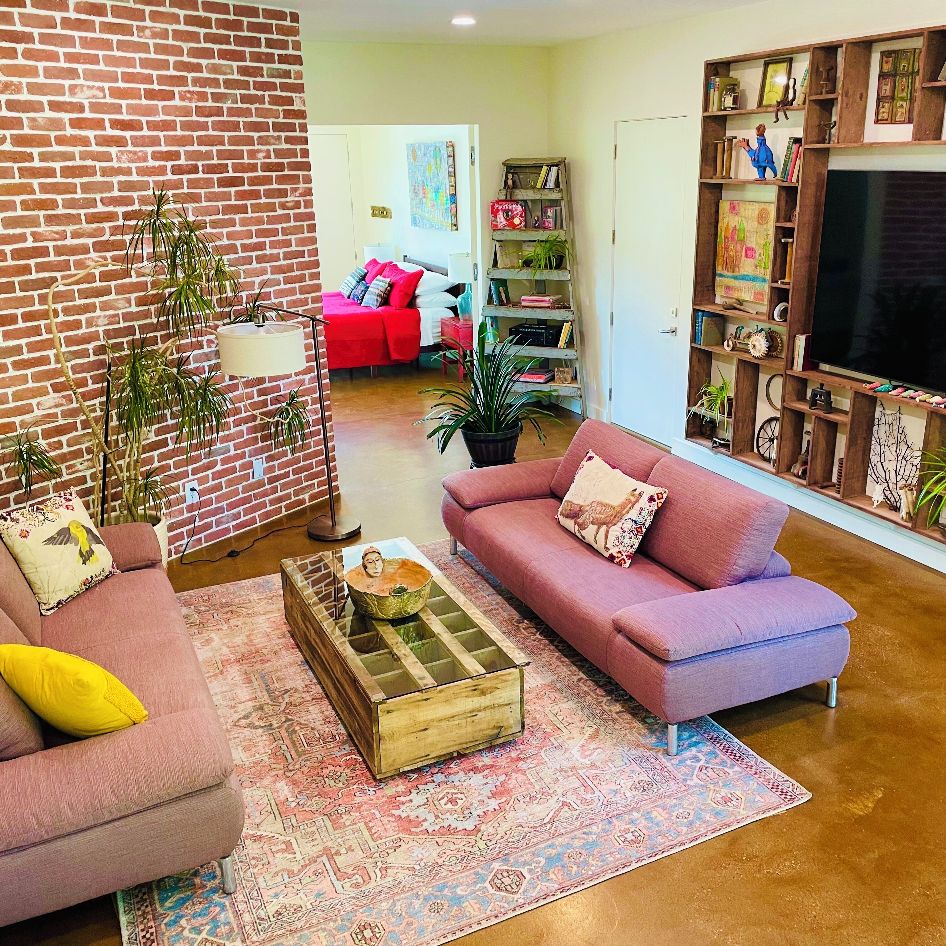 A living room with a brick wall, a red sofa, a pink sofa, a coffee table, and a bookshelf.