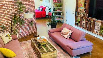 A living room with a brick wall, a red sofa, a pink sofa, a coffee table, and a bookshelf.