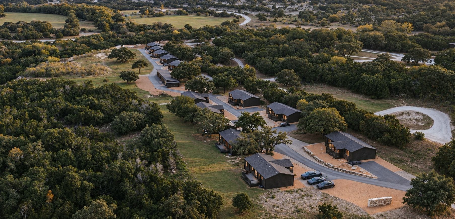 An aerial view of a residential area with multiple houses arranged in a row, surrounded by dense greenery.