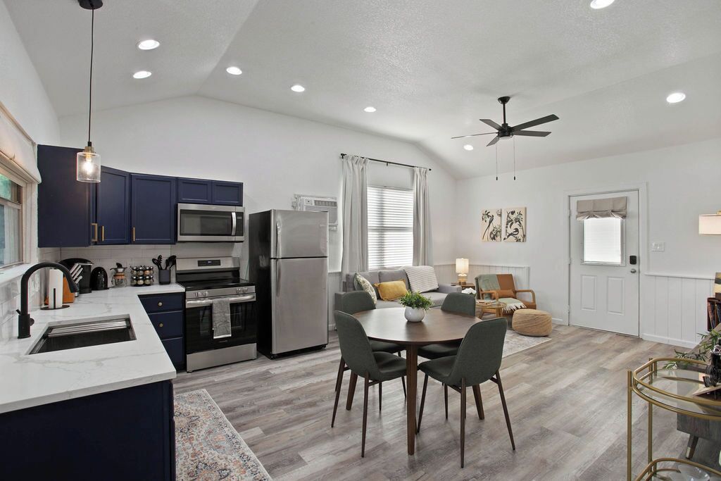 A modern kitchen with dark blue cabinets, stainless steel appliances, and a dining area with a round table and chairs.