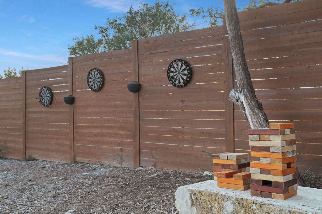A wooden fence with three dartboards mounted on it and a stack of wooden blocks.