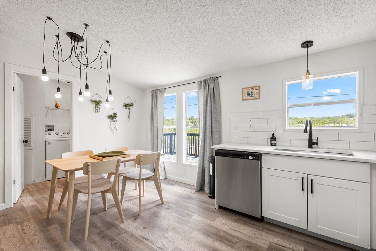 A modern kitchen with white cabinets, a wooden dining table, and a hanging light fixture.