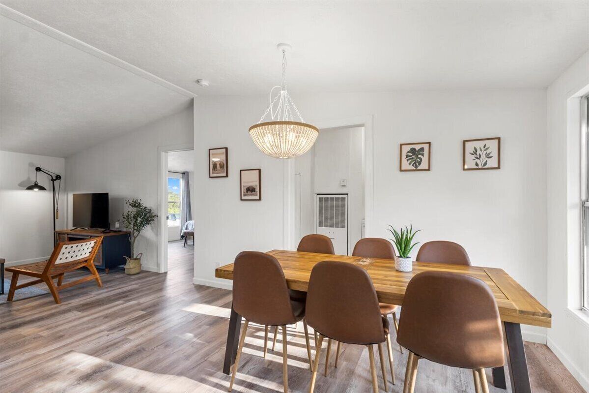 A spacious dining area with a wooden table and brown chairs, a hanging light fixture, and framed artwork on the walls.