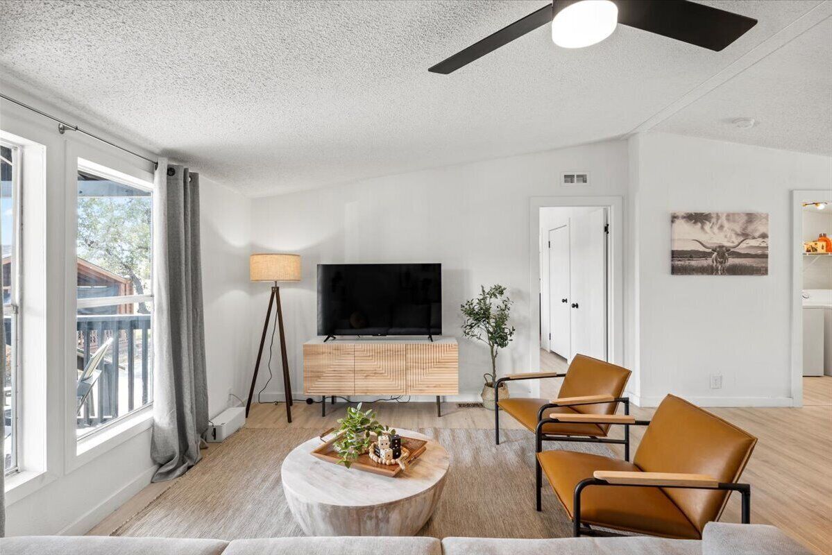 Una sala de estar moderna con un televisor de pantalla plana, un mueble de madera, sillas de cuero y una mesa de centro redonda.