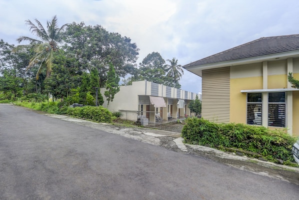 A building with a beige exterior and a flat roof, surrounded by lush greenery and palm trees.