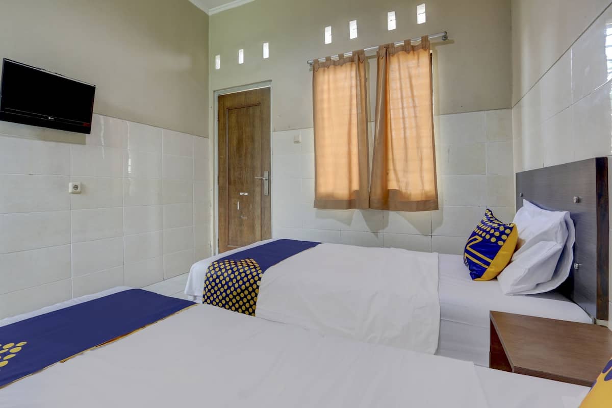 Ein Hotelzimmer mit zwei Betten, einem an der Wand befestigten Flachbildfernseher und einem Fenster mit Vorhängen.