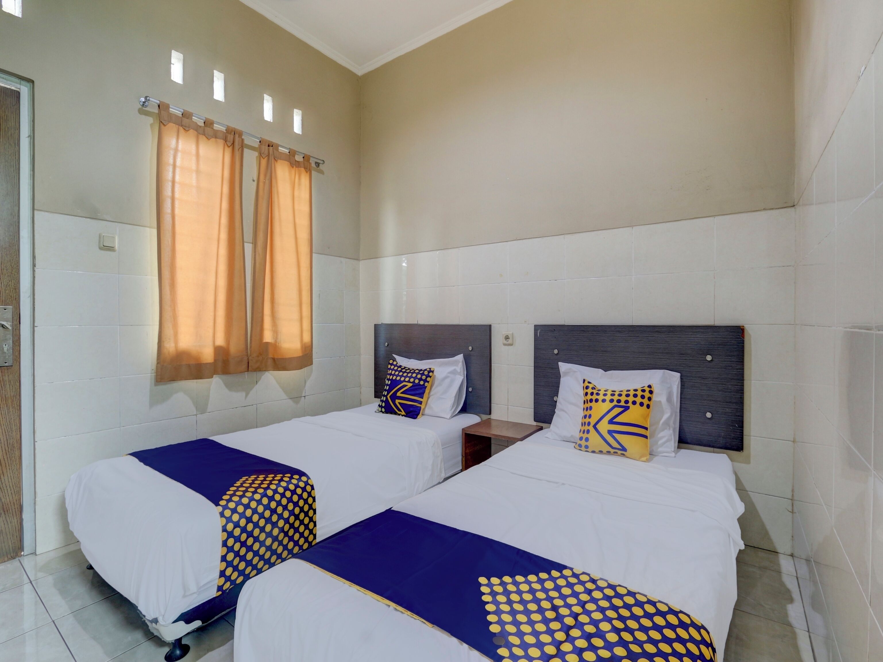 Une chambre d’hôtel avec deux lits, une fenêtre avec des rideaux et un mur recouvert de carreaux.