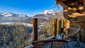 Eine Holzhütte mit Tisch und Stühlen mit Blick auf ein verschneites Gebirge.