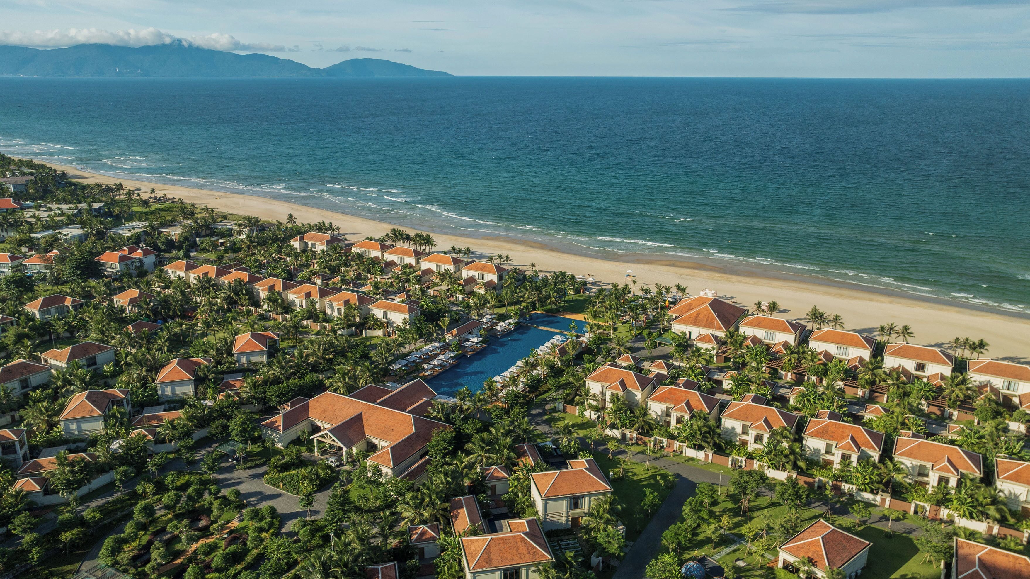 A resort with multiple bungalow-style buildings, a central swimming pool, and a beach view.