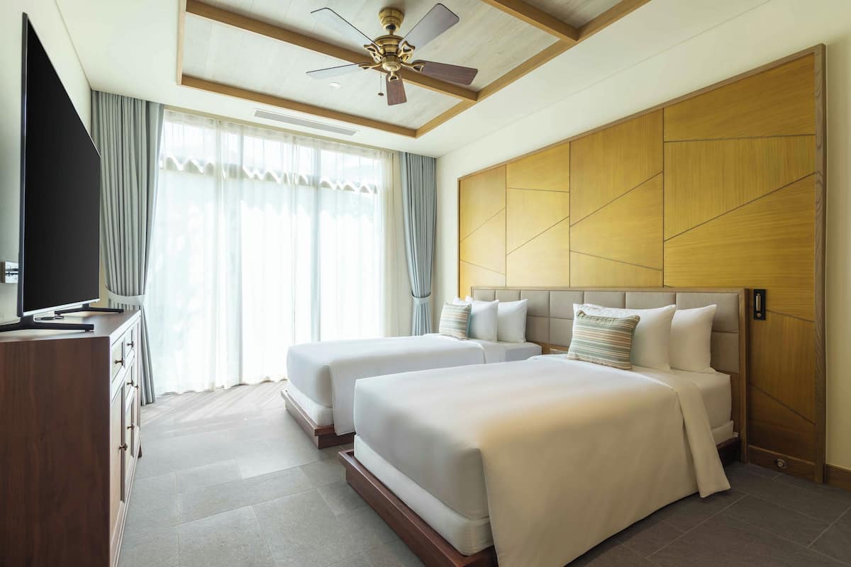 A hotel room with two beds, a TV, and a ceiling fan.