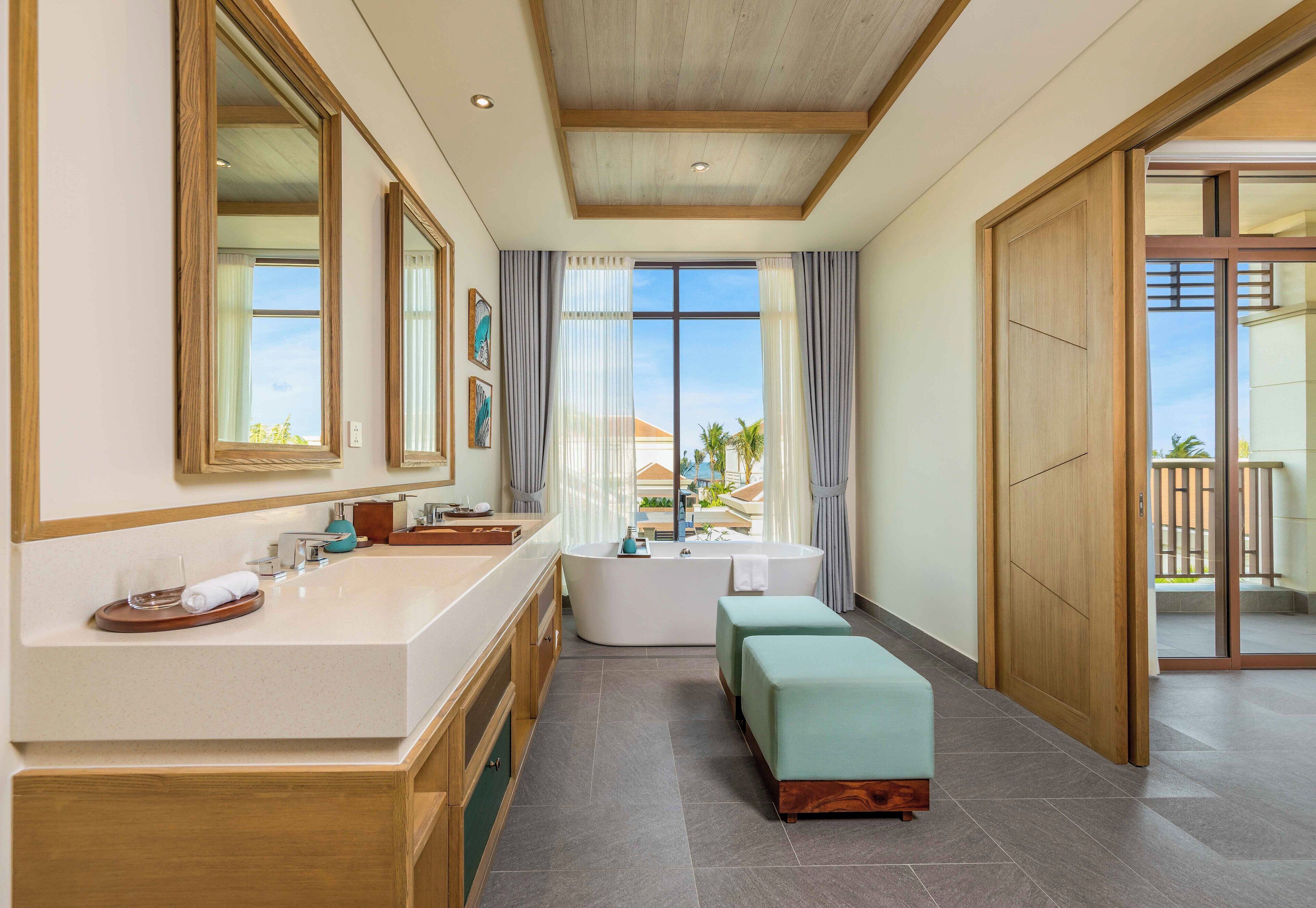 A modern bathroom with a large bathtub, a vanity with a mirror, and a bench.