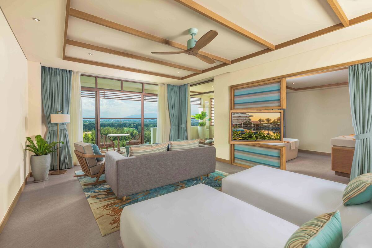 A modern hotel room with a large bed, a sofa, a dining area, and a balcony with a view.