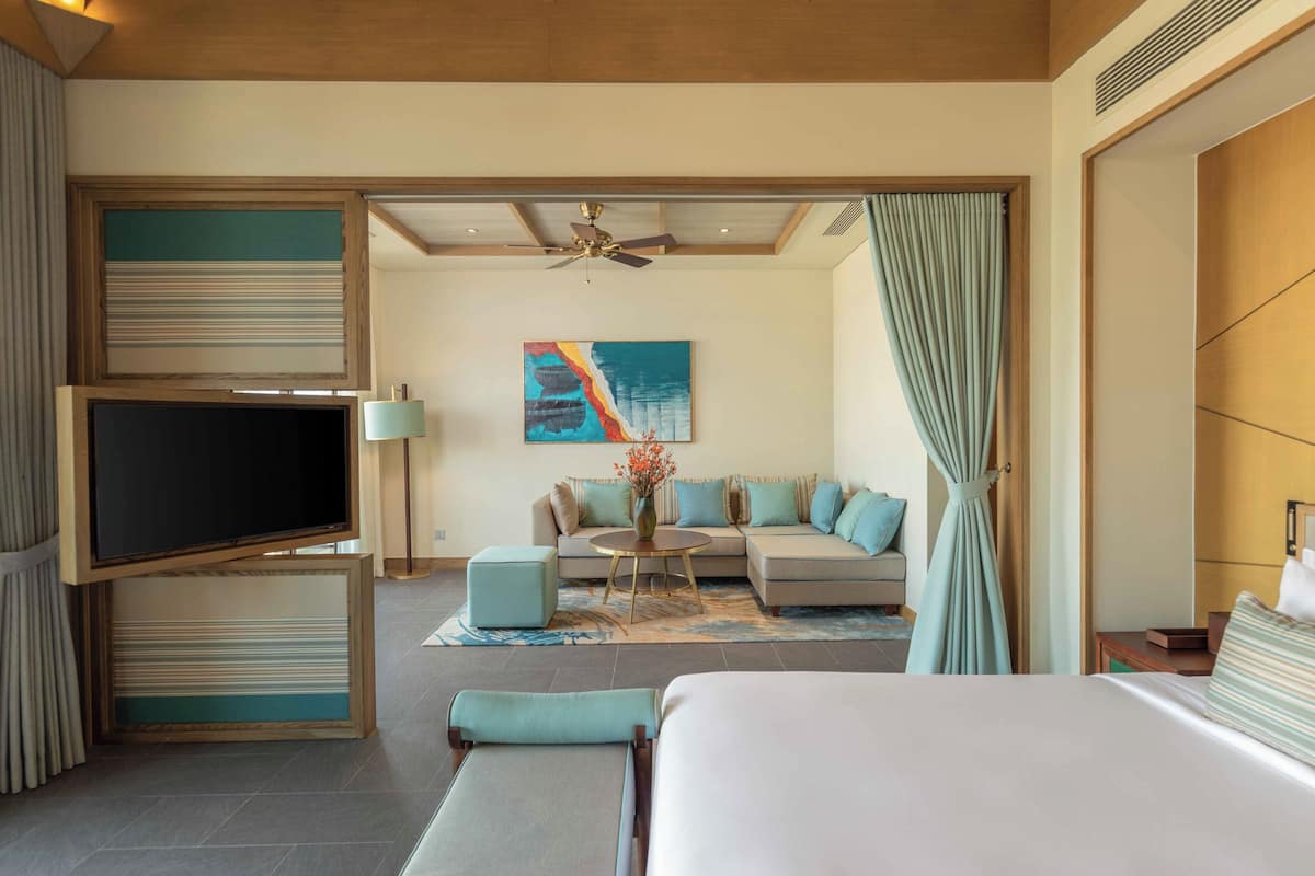 A hotel room with a bed, a TV, a sofa, a coffee table, and a ceiling fan.