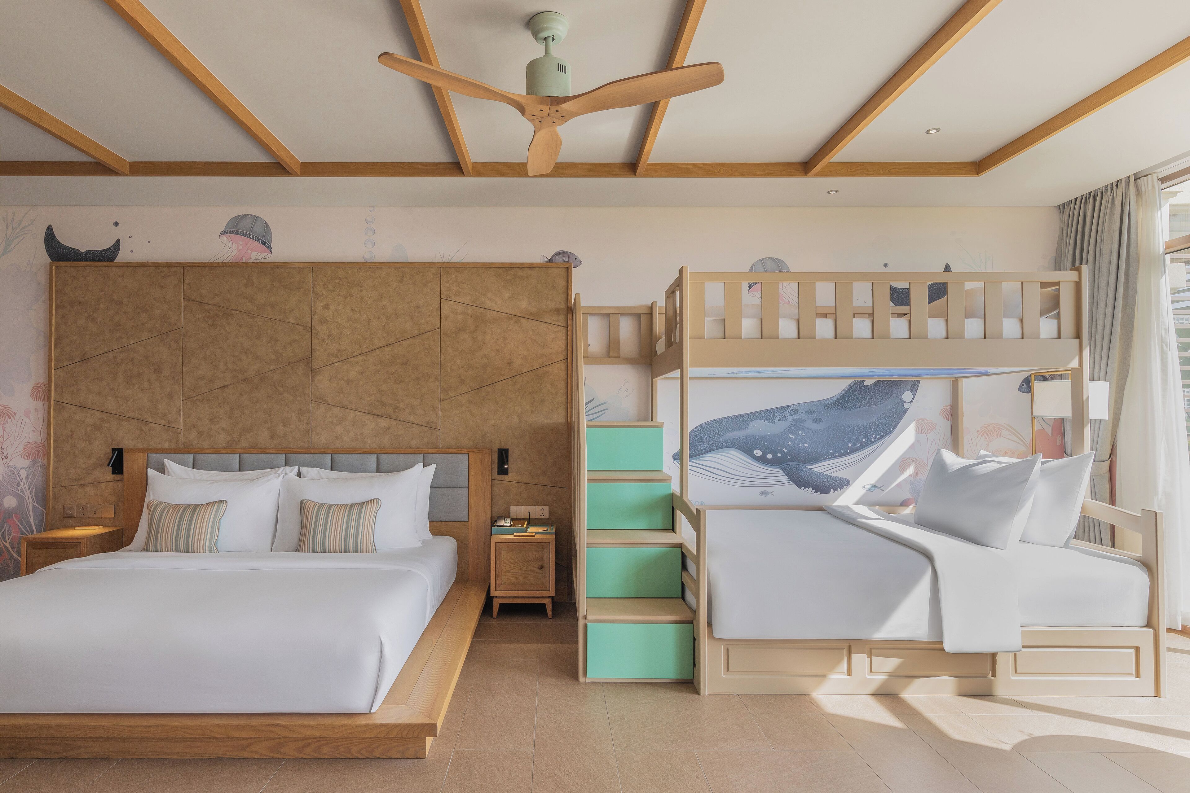 A bedroom with a large bed, a bunk bed, a wooden ceiling fan, and a nightstand with a lamp.