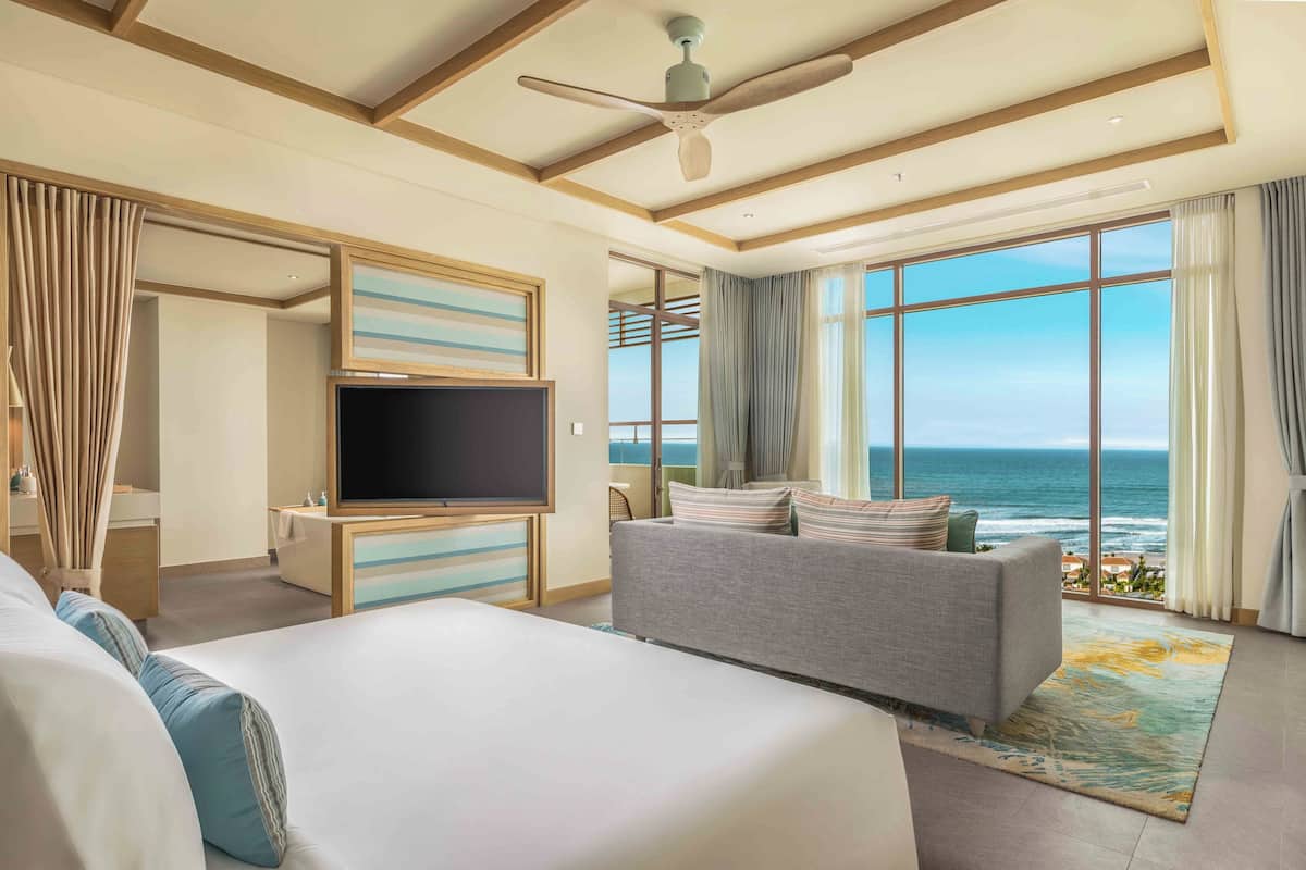 A hotel room with a large bed, a sofa, a TV, and a view of the ocean.