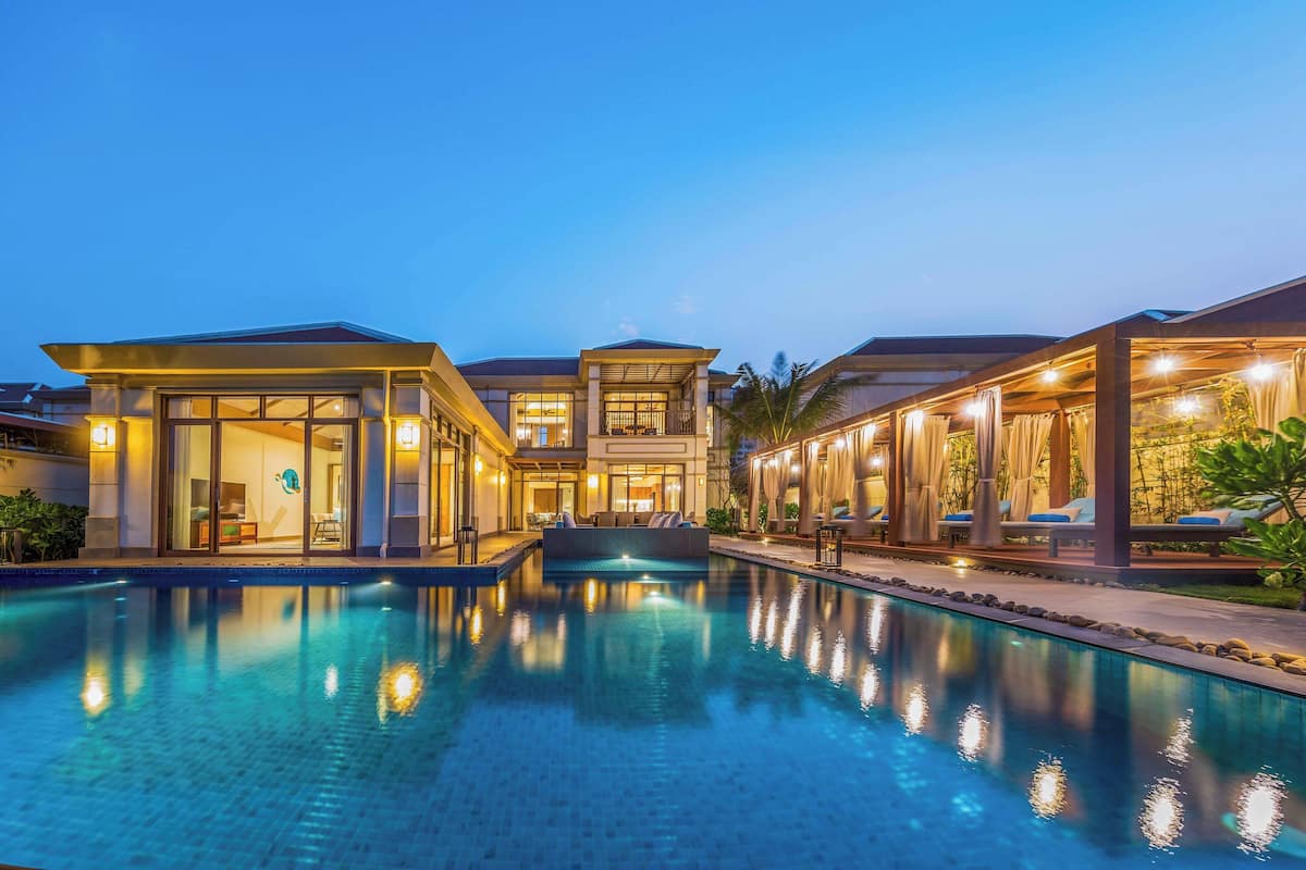 A modern hotel with a swimming pool, large windows, and outdoor seating areas.