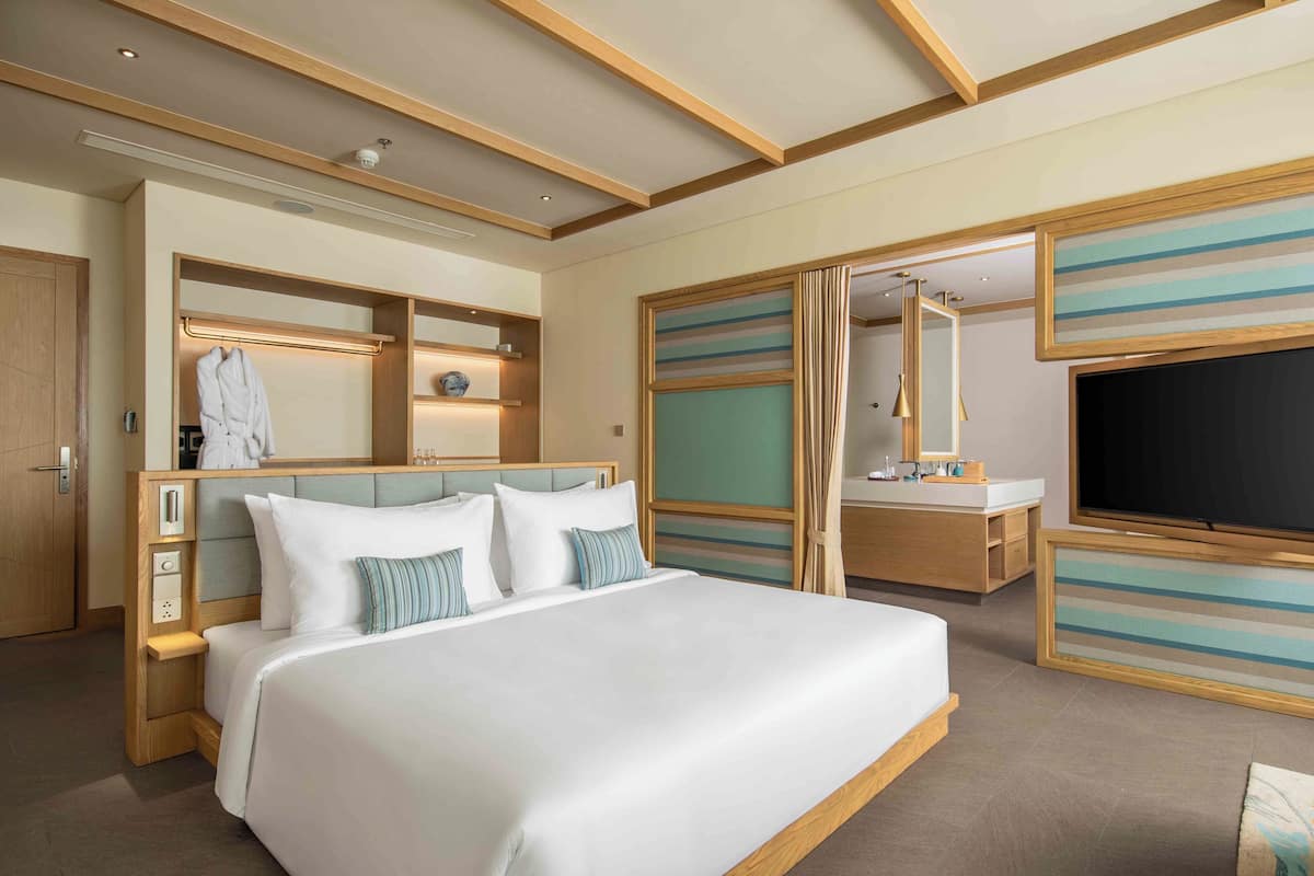 A modern hotel room with a large bed, a built-in wardrobe, a vanity with a mirror, and a flat-screen TV.