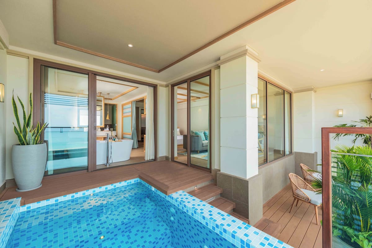 A modern indoor pool area with a tiled floor, wooden deck, and glass doors leading to a living space.