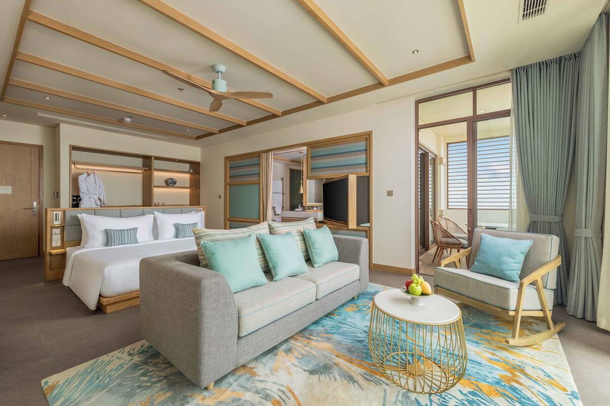 A hotel room with a large bed, a sofa, a rocking chair, and a small table with fruit.