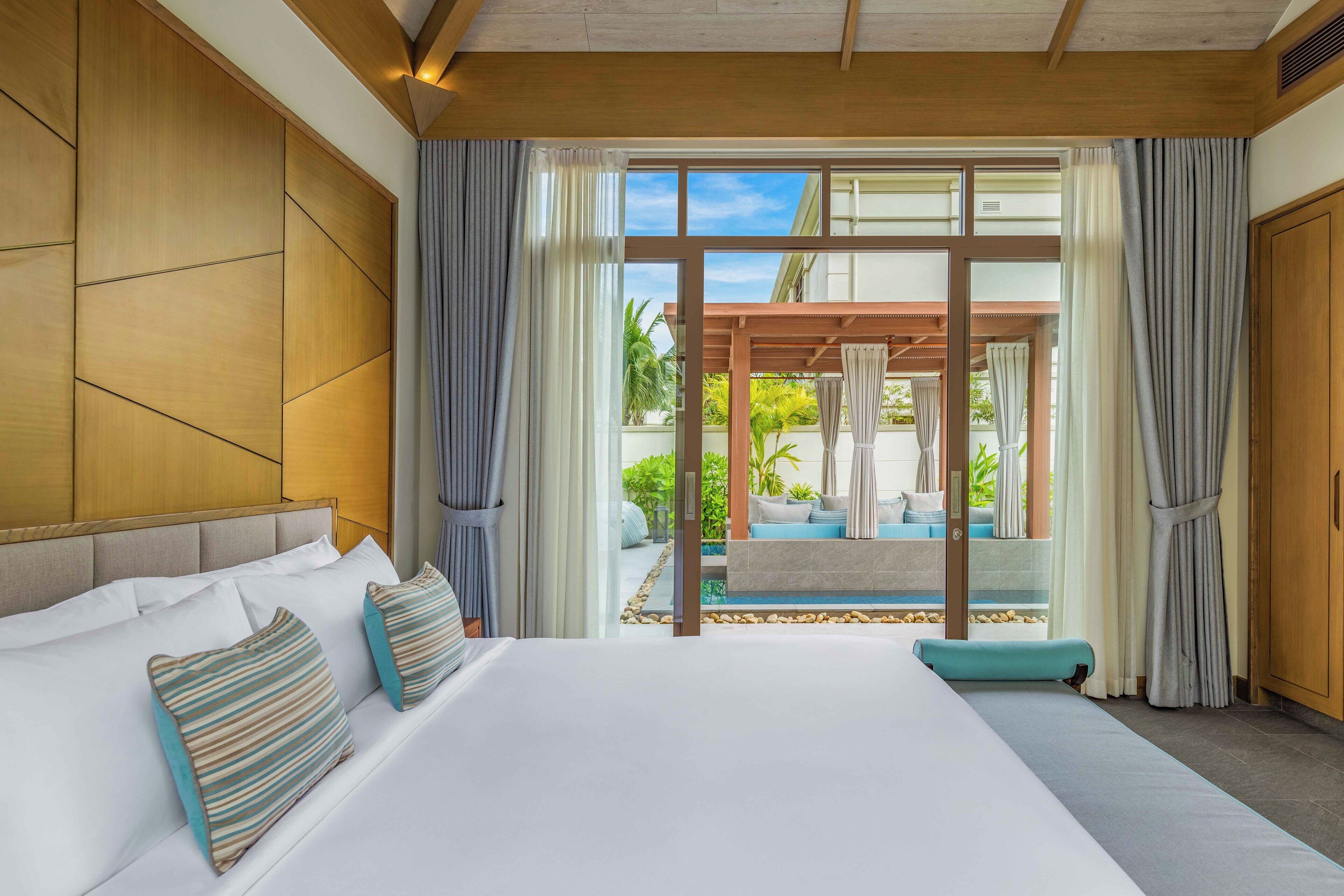 Habitación de hotel con una cama grande, vistas a una piscina y zona exterior, y paneles de madera en las paredes.
