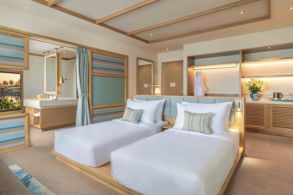 A hotel room with two beds, a large mirror, a vanity with a sink, and a view of the outdoors.