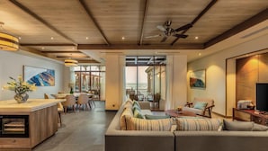 A spacious living area with a large sofa, dining table, and chairs. There is a kitchen area with a countertop and a built-in oven. The room has wooden beams on the ceiling and large windows offering a view of the ocean. - Fusion Resort & Villas Da Nang (Da Nang)
