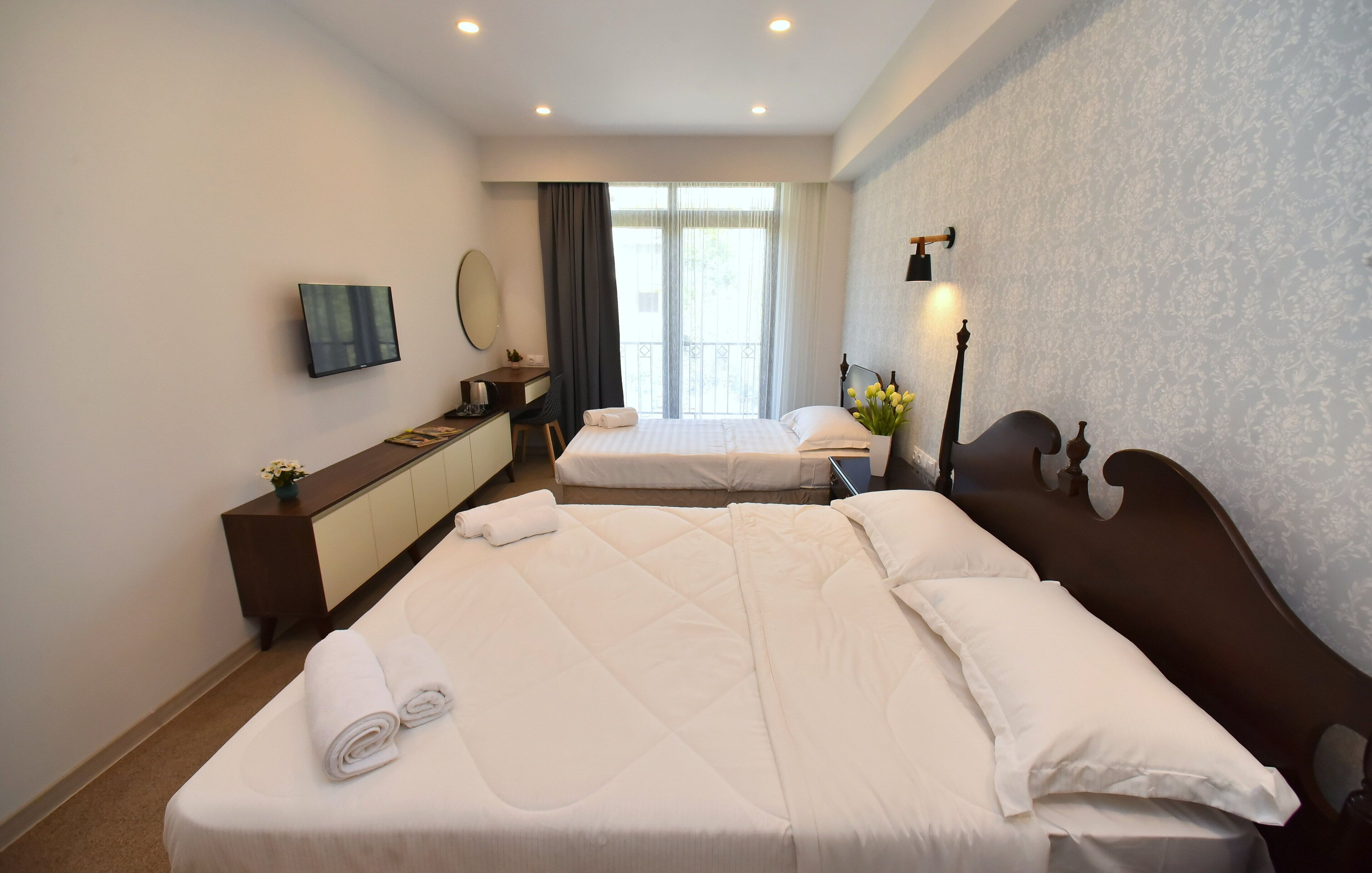Habitació d'hotel amb dos llits, escriptori, cadira, televisió i finestra amb cortines.