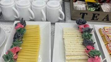 Una mesa de buffet con tazas blancas, una bandeja de queso amarillo y blanco, y una bandeja de queso blanco y rosa.