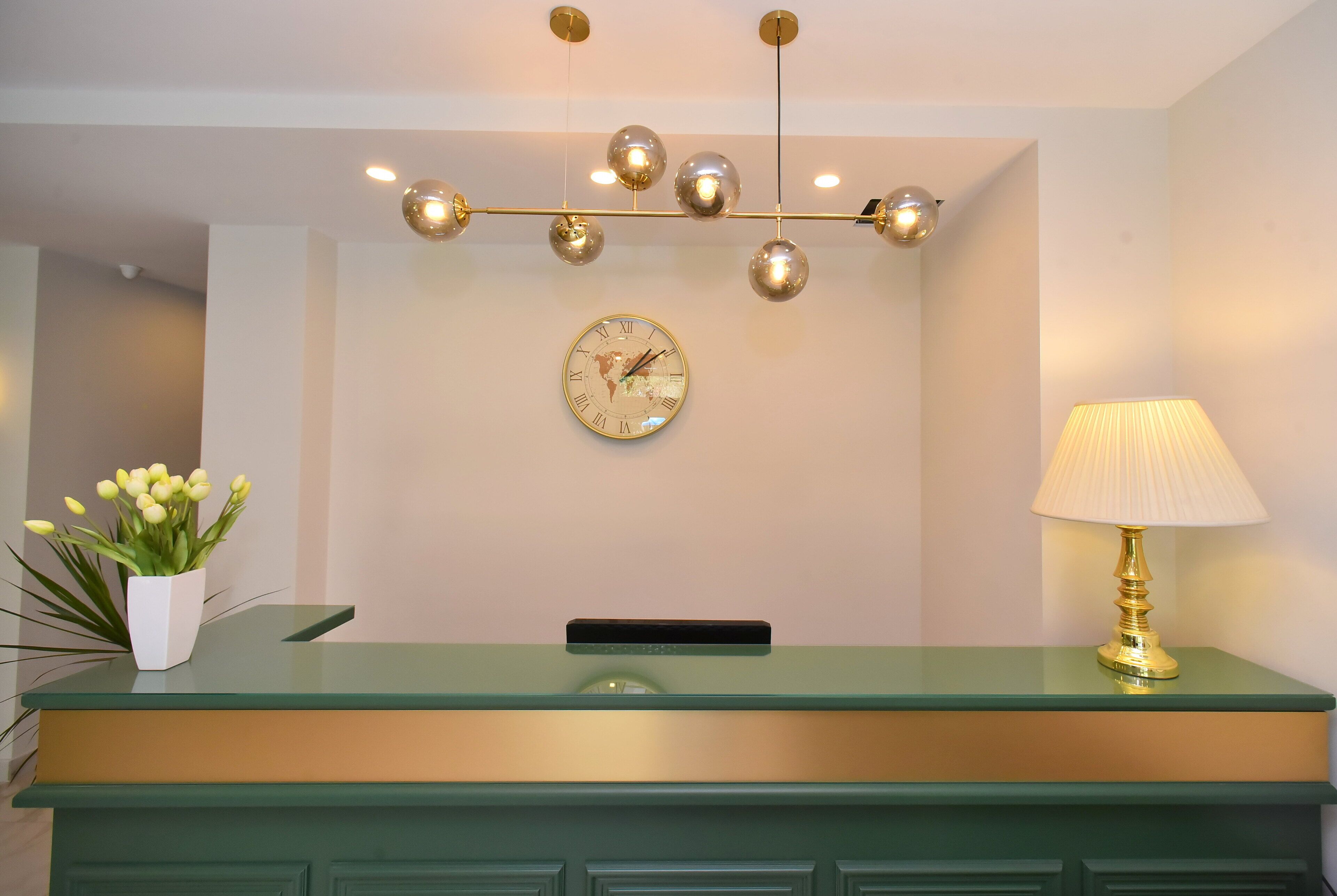 A reception desk with a green top, a gold lamp, a globe clock, and a plant.