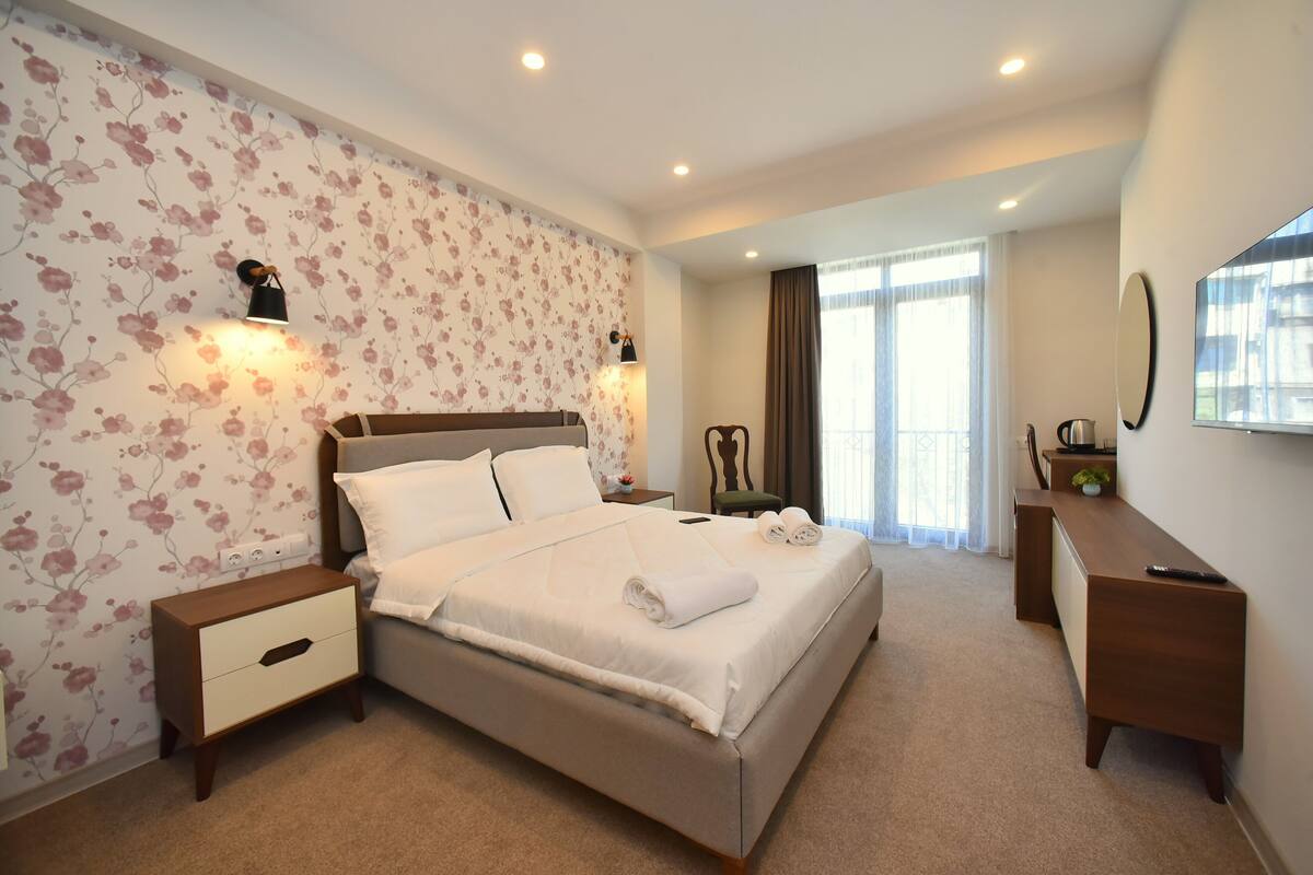 A hotel room with a large bed, a nightstand, a dresser, and a mirror.