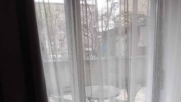 Una habitación con un gran ventanal cubierto por cortinas translúcidas, una pequeña mesa redonda y una silla visibles a través del ventanal.