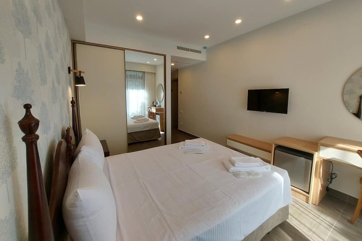 A hotel room with a large bed, a desk, a television, and a mirror.
