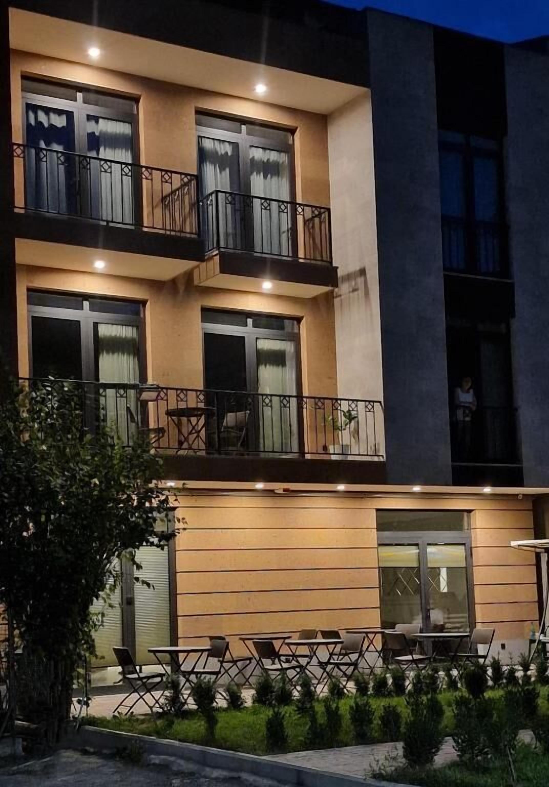A multi-story building with balconies, outdoor seating, and a well-lit entrance.