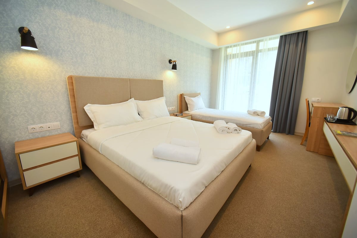 A hotel room with a large bed, a smaller bed, a desk with a chair, and a nightstand.