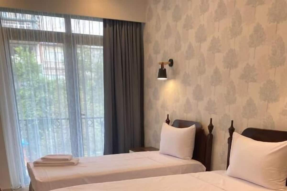 A hotel room with two single beds, a nightstand, a lamp, and a window with curtains.