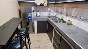 Une cuisine compacte avec des meubles de rangement sombres, un évier, une bouilloire et un petit plan de travail.
