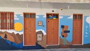 Un bâtiment doté de trois portes en bois, chacune ayant une fenêtre. Un mur est décoré d’une fresque représentant un paysage de montagne avec des arbres, un soleil et des nuages.
