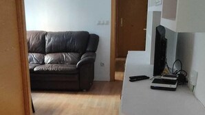 A room with a wooden floor, a black leather sofa, a white cabinet, and a door leading to another room. - M&m Apartament (Madrid)