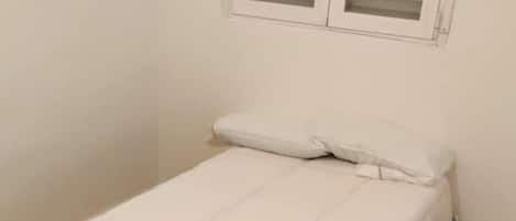 A small, single-bed room with a wooden floor, white walls, and a window with blinds.