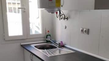 Una cocina con un lavamanos de acero inoxidable, horno empotrado y una ventana con persianas.