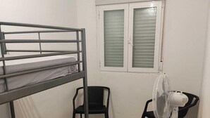 A bunk bed, a desk with a chair, a standing fan, and a window with blinds. - M&m Apartament (Madrid)