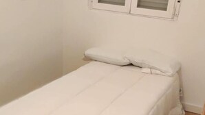 A small, single-bed room with a wooden floor, white walls, and a window with blinds. - M&m Apartament (Madrid)