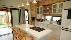 A modern kitchen with a central island, white cabinets, and a brick accent wall. - Refúgio da Ibiraquera Jacuzzi e Vista (Imbituba)