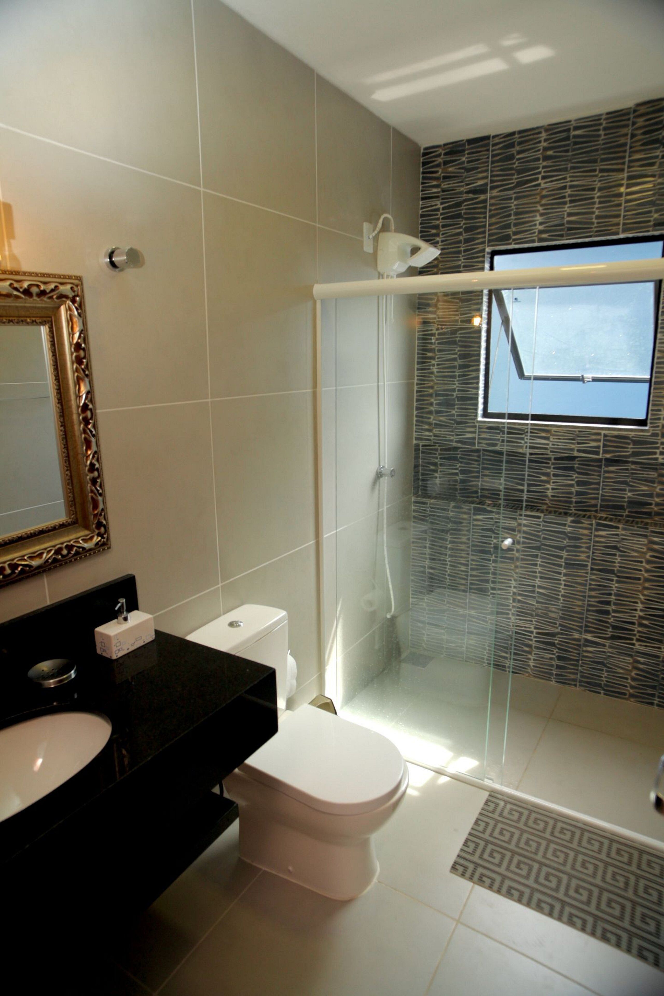 A bathroom with a glass-enclosed shower, a white toilet, a black sink, and a mirror with a decorative frame.
